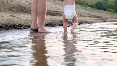 婴儿穿着尿布沿着河岸走第一步，洒上水，和母亲<strong>一起</strong>散步。 腿。 特<strong>写</strong>